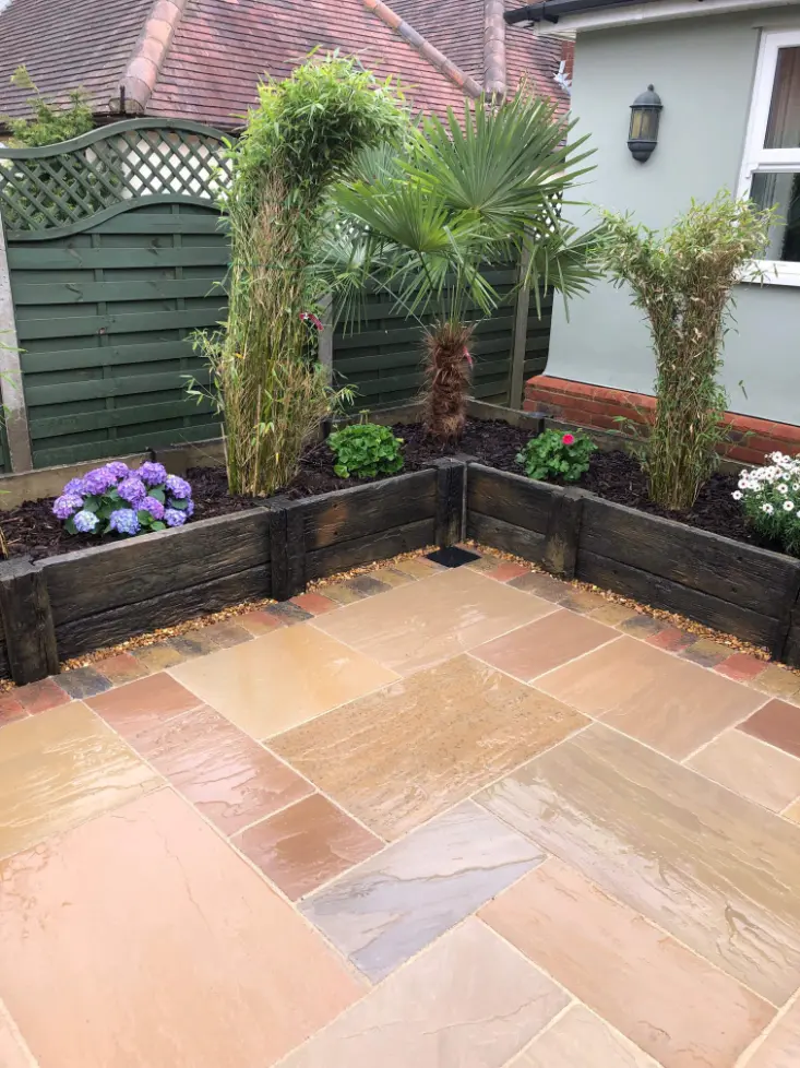 Wet corner garden patio with multicolored paving stones and raised wooden planters filled with palms, bamboo, and flowers.