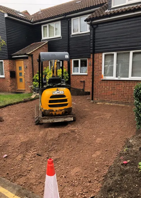 Yellow JCB digger on a freshly dug driveway in front of a British semi-detached house with black cladding and brick walls.