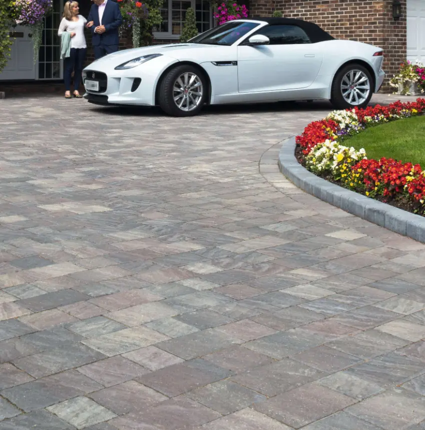 White convertible Jaguar parked on gray and brown stone driveway next to flower bed with red, yellow, and white flowers.