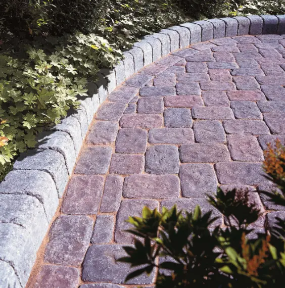 Curved garden pathway with purple cobblestone pavers bordered by grey stone edging and surrounded by green plants.