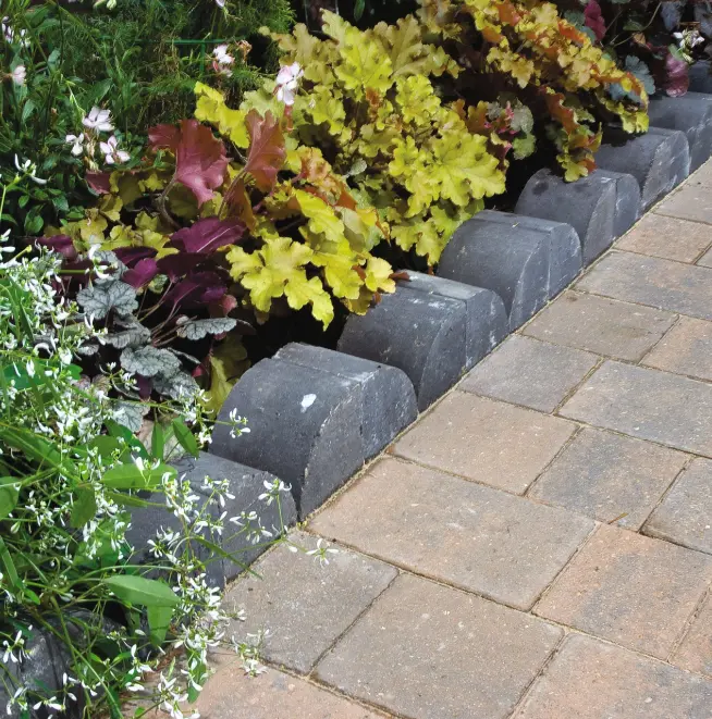 Black stone edging bordering a flower bed with colorful foliage, next to beige and grey stone paving slabs.